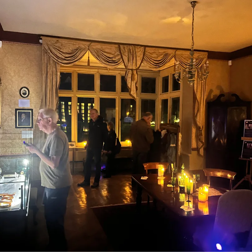 Visitors in a candlelit historic room at Gilbert White's House, with a chandelier and tall leaded windows
