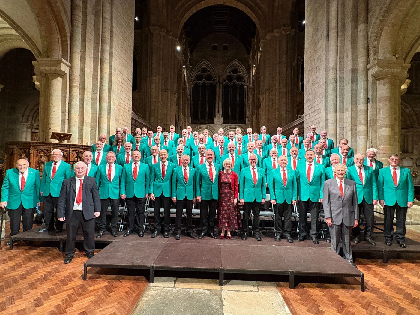 Romsey Male Voice Choir in green blazers and red ties on staging in a cathedral nave