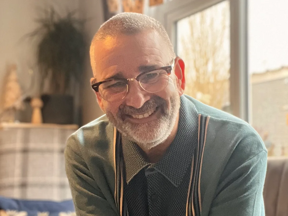 Rob Fielder in glasses and a green cardigan, smiling at the camera in a living room
