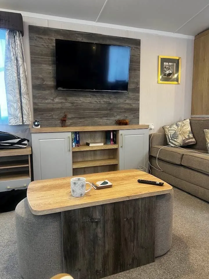 Living room of a mobile home with a wall-mounted television, a wooden coffee table and a grey sofa