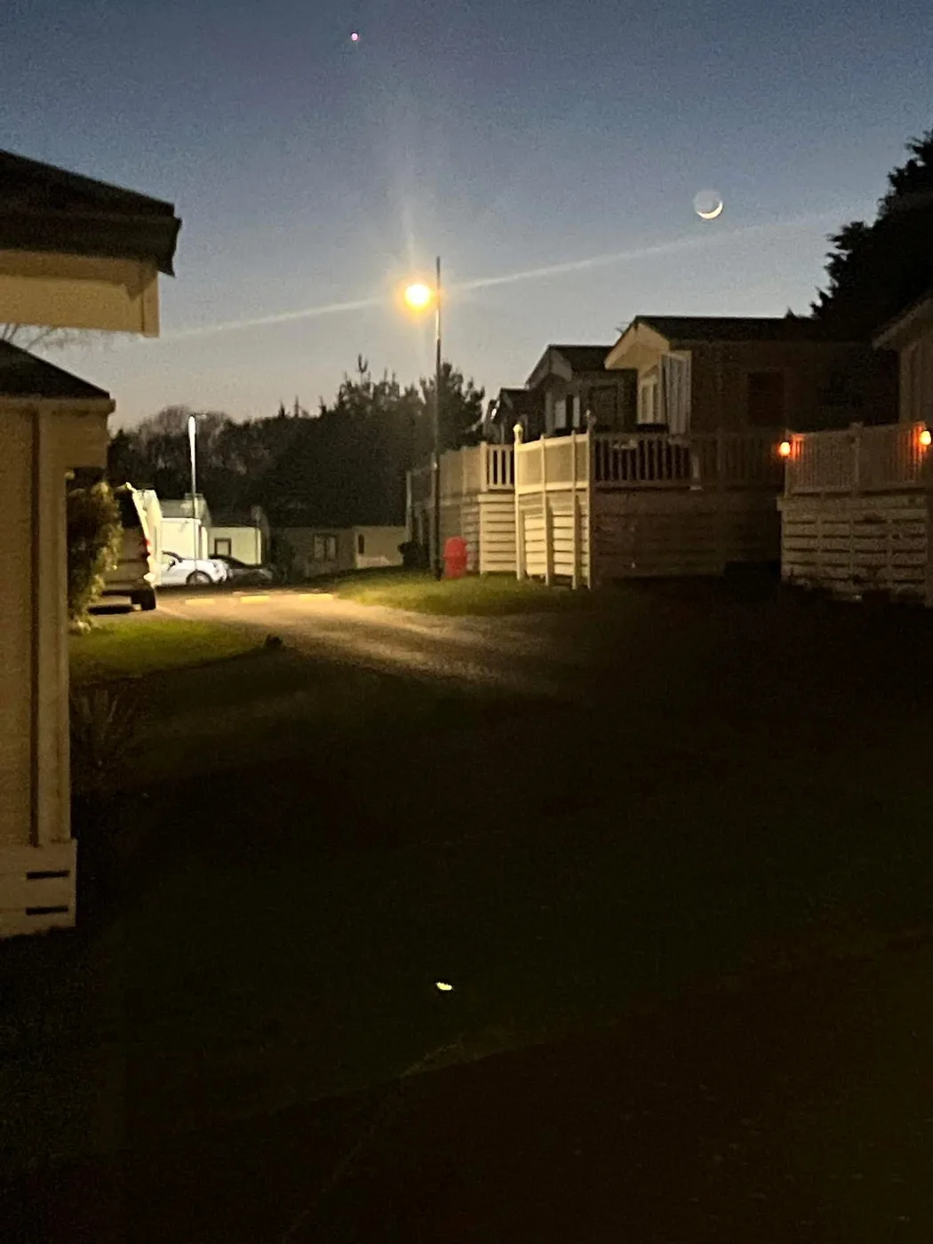 Holiday homes and a street lamp at dusk, with a crescent moon in the sky
